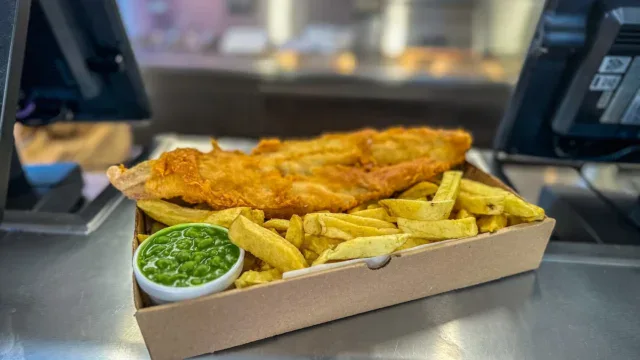 Freshly cooked fish and chips served with mushy peas in a takeaway box at Fleckney.Today. Perfect for a traditional British fish and chips experience.
