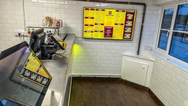 Fleckney fish and chips shop counter with menu board, cash register, and window view, showcasing a clean and modern takeaway restaurant environment.