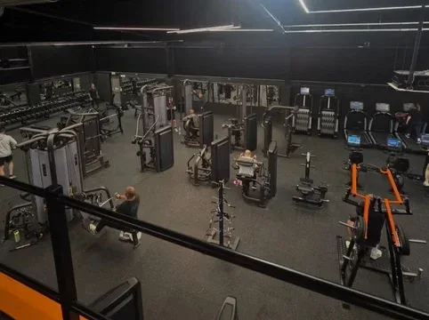 Modern gym with various fitness equipment including cardio machines, weight stations, and strength training gear in a spacious, well-lit environment.