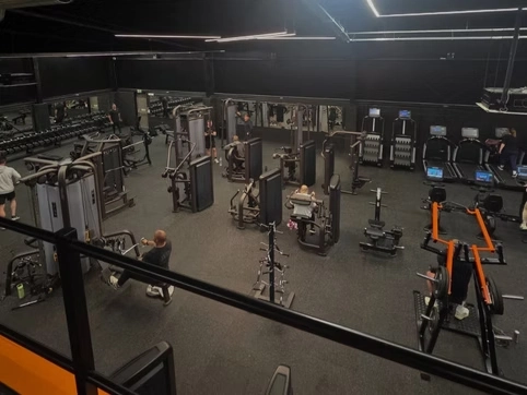 Modern gym with various fitness equipment including cardio machines, weight stations, and strength training gear in a spacious, well-lit environment.