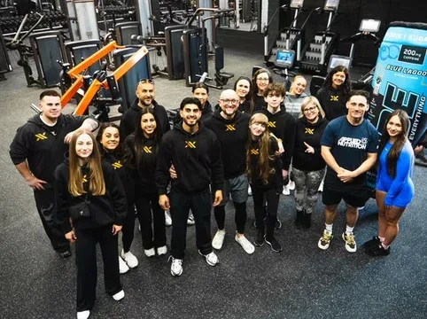 Group of diverse people in workout gear standing together in a gym, smiling after a fitness class, promoting health and community engagement.