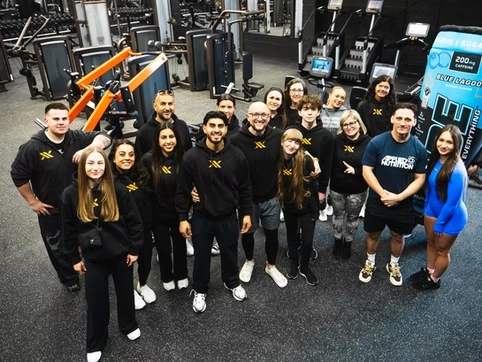 Group of diverse people in workout gear standing together in a gym, smiling after a fitness class, promoting health and community engagement.
