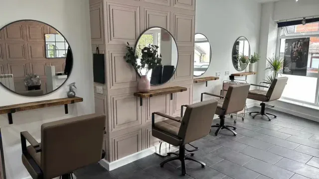 Stylish hairdressing salon with contemporary styling stations, large mirrors, and comfortable chairs, creating a welcoming environment for clients seeking professional haircuts and treatments.