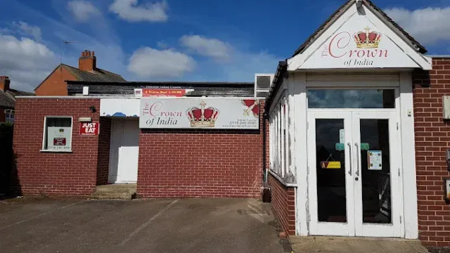 Indian restaurant "Crown of India" with signage and entrance in Fleckney, showcasing a brick building with a white door and a prominent sign featuring a crown logo.