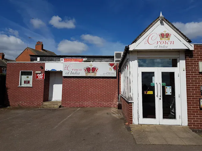 Indian restaurant "Crown of India" with signage and entrance in Fleckney, showcasing a brick building with a white door and a prominent sign featuring a crown logo.