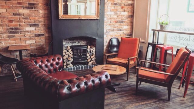A welcoming lounge area featuring a brick wall, a fireplace, and comfortable seating including leather and fabric chairs, creating a warm and inviting atmosphere.