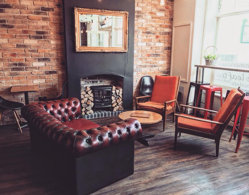 A welcoming lounge area featuring a brick wall, a fireplace, and comfortable seating including leather and fabric chairs, creating a warm and inviting atmosphere.