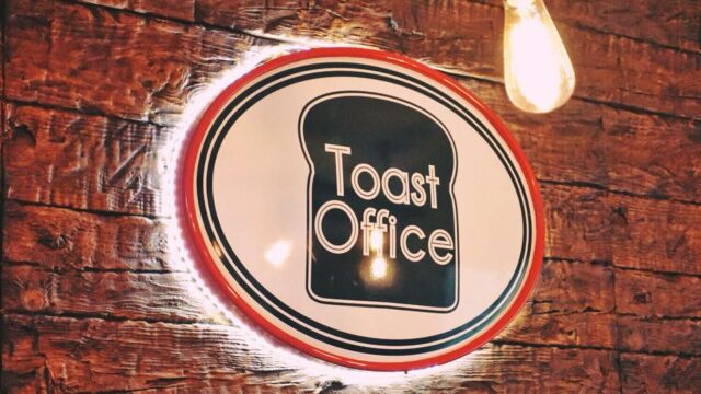 Sign for Toast Office mounted on a rustic brick wall, featuring a retro design with a slice of toast illustration and bold lettering. Perfect for a bakery or café branding.
