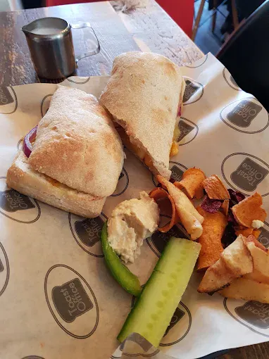 Fish finger sandwich with chips, cucumber, and tartar sauce on a wooden table.