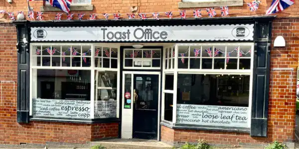 Exterior view of Fleckney Toast Office, a charming local café with patriotic decorations, offering coffee, tea, and snacks in a welcoming setting.
