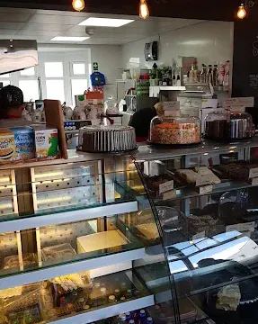 Modern bakery and coffee shop interior with display cases, baked goods, and a cozy atmosphere illuminated by hanging light bulbs.