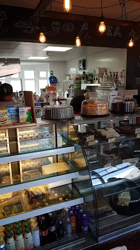 Modern bakery and coffee shop interior with display cases, baked goods, and a cozy atmosphere illuminated by hanging light bulbs.