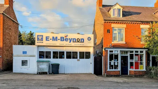 Auto repair shop E-M Beynon in Fleckney with signage, garage door, and surrounding buildings under a blue sky.