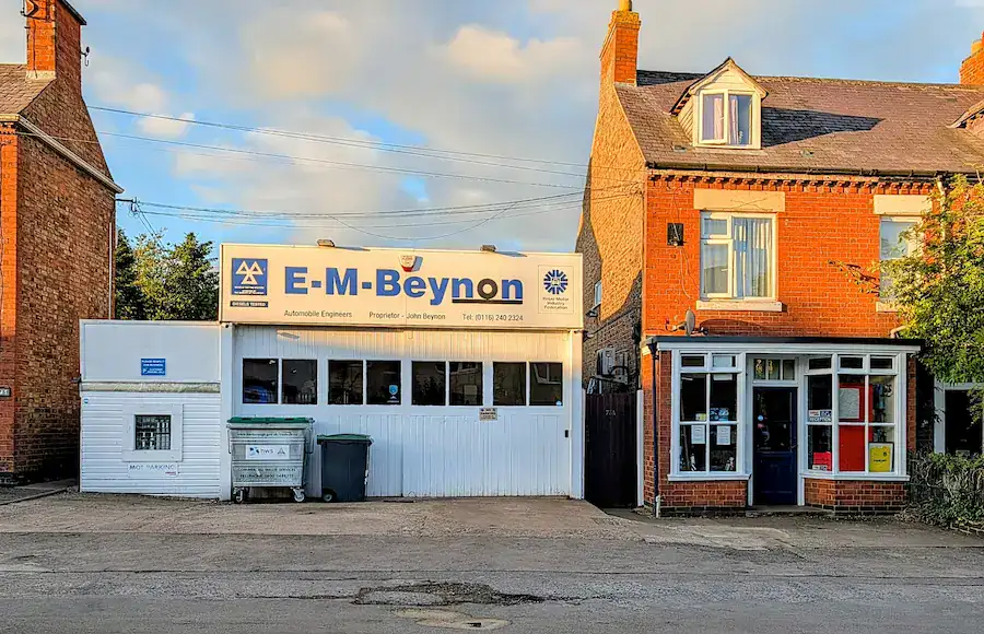 Auto repair shop E-M Beynon in Fleckney with signage, garage door, and surrounding buildings under a blue sky.